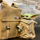 An excited Baby Yoda figure from Star Wars The Mandalorian gazes longingly at a highly-detailed messenger pouch that will soon be his home.